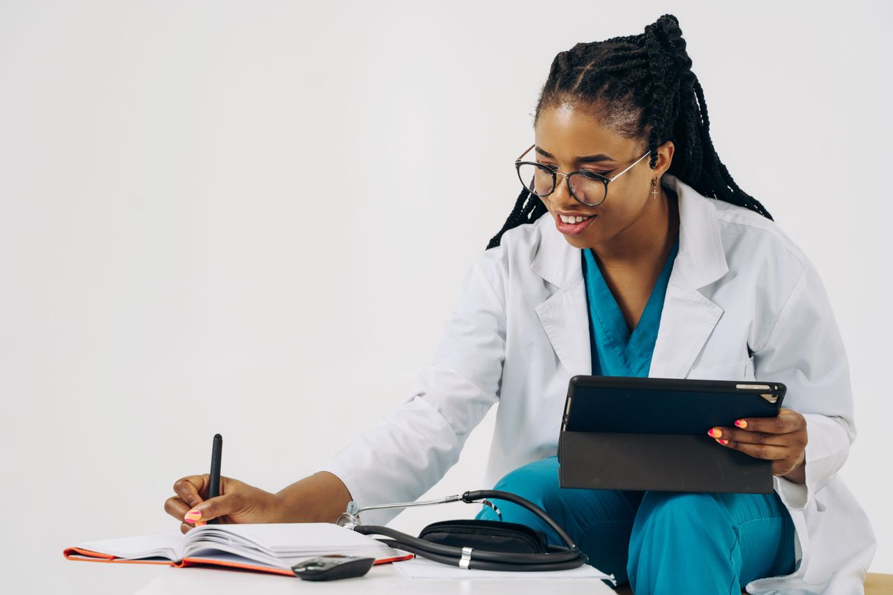 Smiling female doctor in scrubs using tablet and taking notes in a healthcare setting.