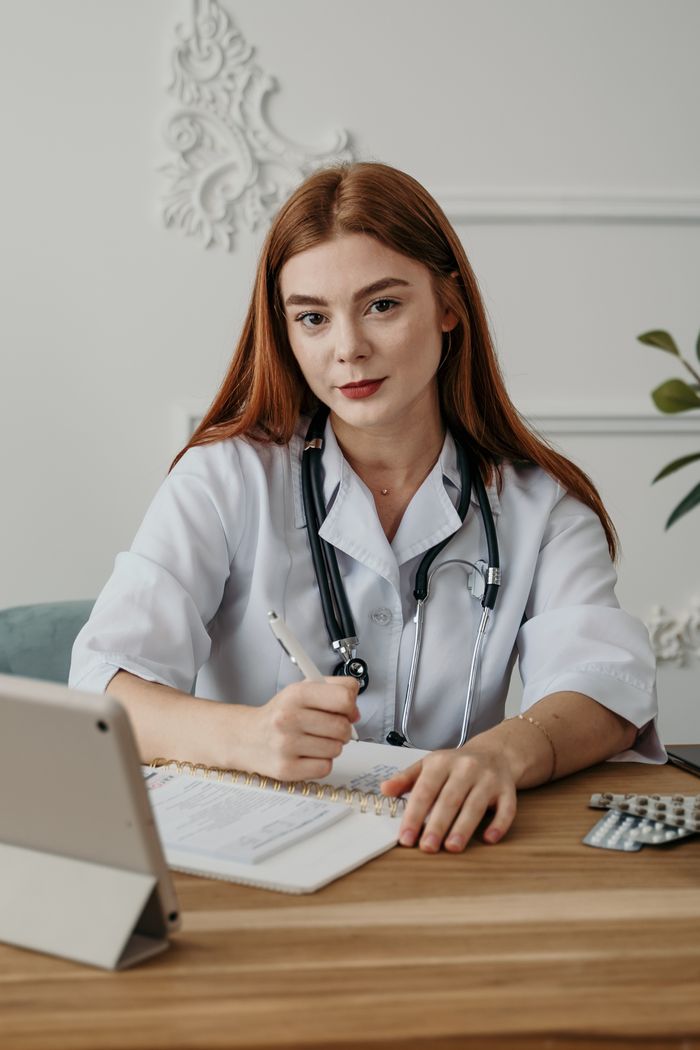 Services Portrait of a young female doctor with stethoscope, taking notes at her desk with an electronic tablet.